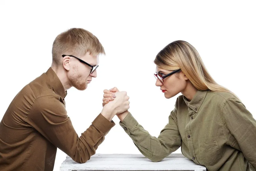 Un homme et une femme s’affrontent au bras de fer, face à face, le regard déterminé.