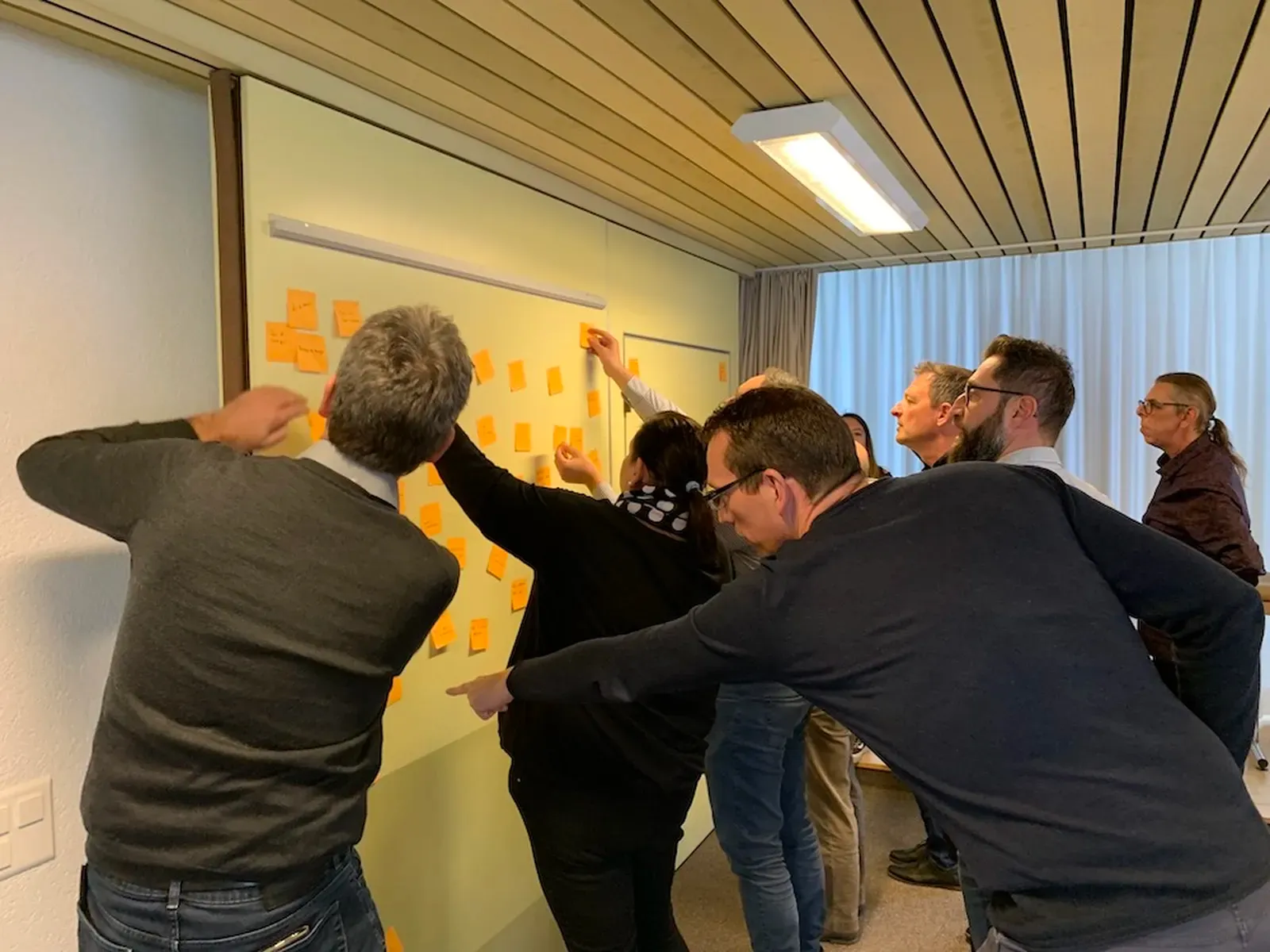 Un groupe de personnes colle des notes adhésives orange sur un mur pendant un atelier.